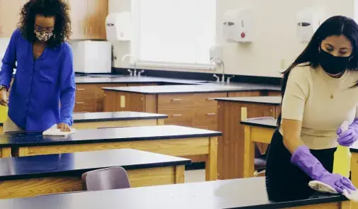 teachers with mask and gloves on disinfect desks