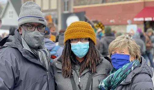 three people, Fed Ingram, Marcia Howard, and Randi Weingarten stand in George Floyd Square