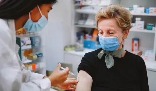 doctor giving woman vaccine. they both wear masks