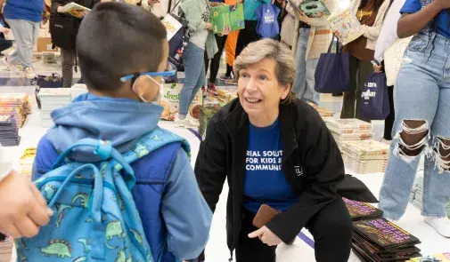 AFT President Randi Weingarten crouched to talk with a small child amid piles of free books